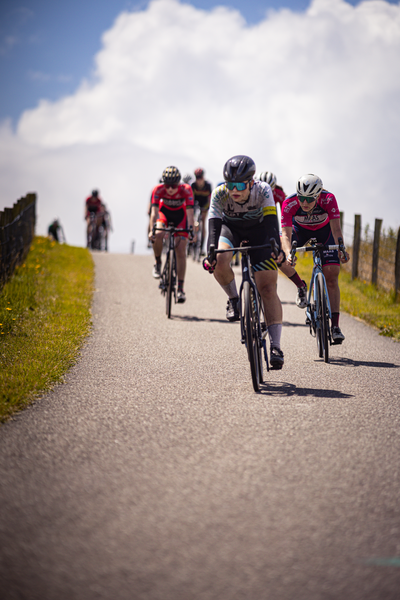 A group of cyclists racing down a road with one wearing the number 19.