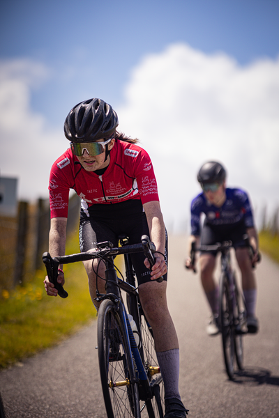 Two cyclists wearing red and blue uniforms race down the road.