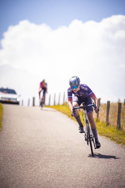 A cyclist wearing a blue helmet races down the road as another cyclist follows behind.