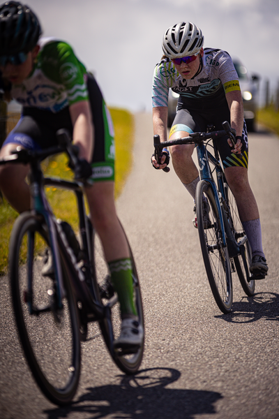 Two cyclists are racing on a track, one in green and blue and the other with black and white.