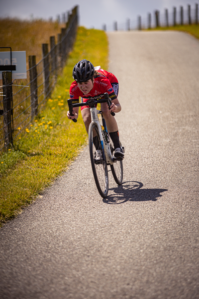 A young man in a red shirt is riding a bike on a paved road.