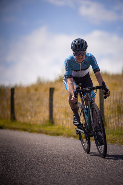 A cyclist wearing a blue and white jersey races down the road.