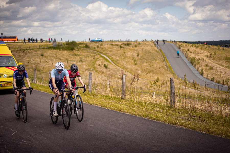 Three people ride bicycles on a road, including a man in a blue shirt.