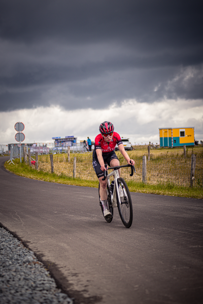 A cyclist in a red jacket and black helmet riding on the road.