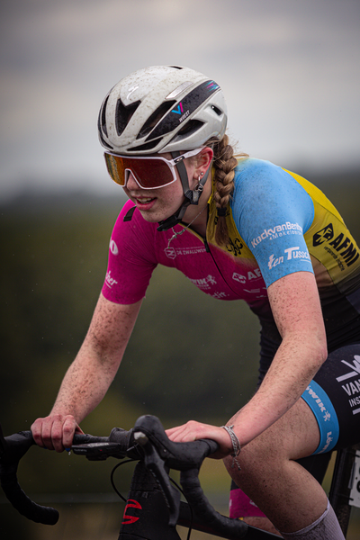 A woman wearing a pink and blue cycling suit is riding a bike.