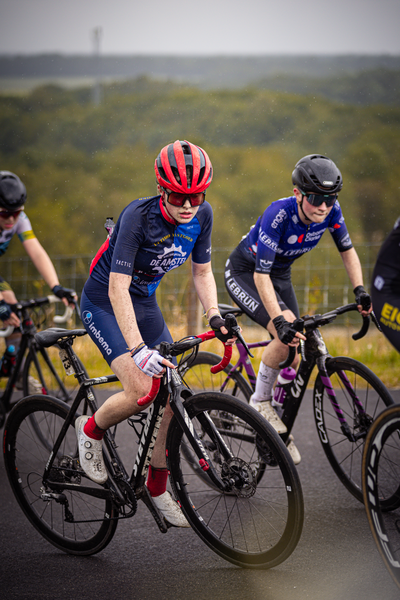 Three cyclists wearing helmets are riding their bikes.