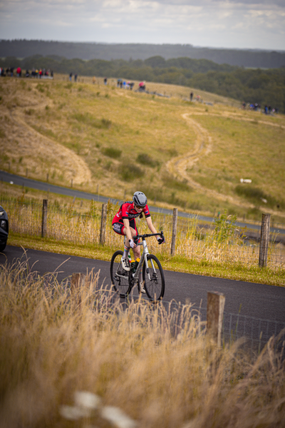 A man wearing a red shirt rides his bicycle on the road near an open field.