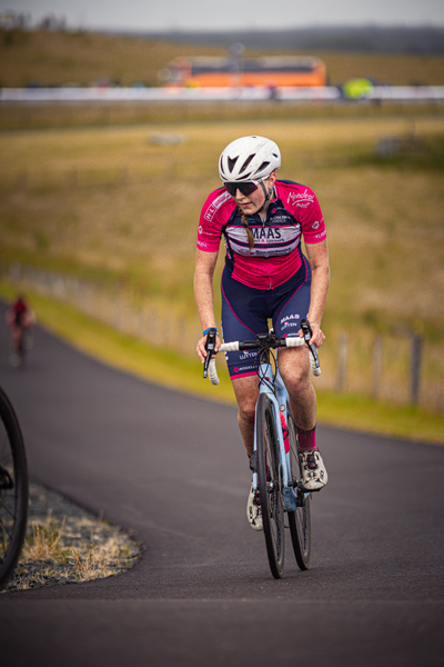 A person in a red and white shirt is riding a blue bike down a race track.