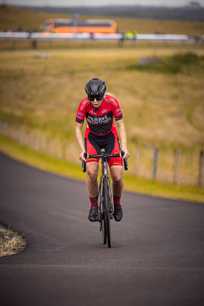 A cyclist rides down a road with the words "Nederlands Kampioenschap" on their shirt.