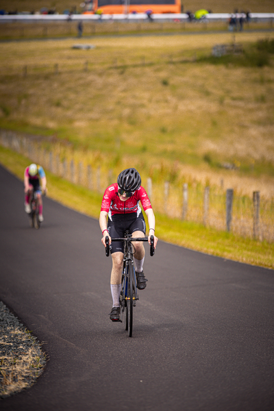 A cyclist on a road with another rider in the background.