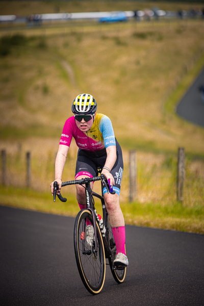 A cyclist in a pink and yellow jersey is riding a black bike on an asphalt road.