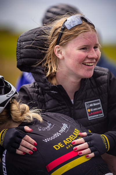 A woman wearing a black jacket is posing for a photo. The words "Nederlands Kampioenschap" are visible on her vest.