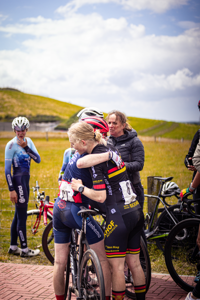 Two women, wearing matching red and black uniforms with the word "Bouwen" on them, hug each other.