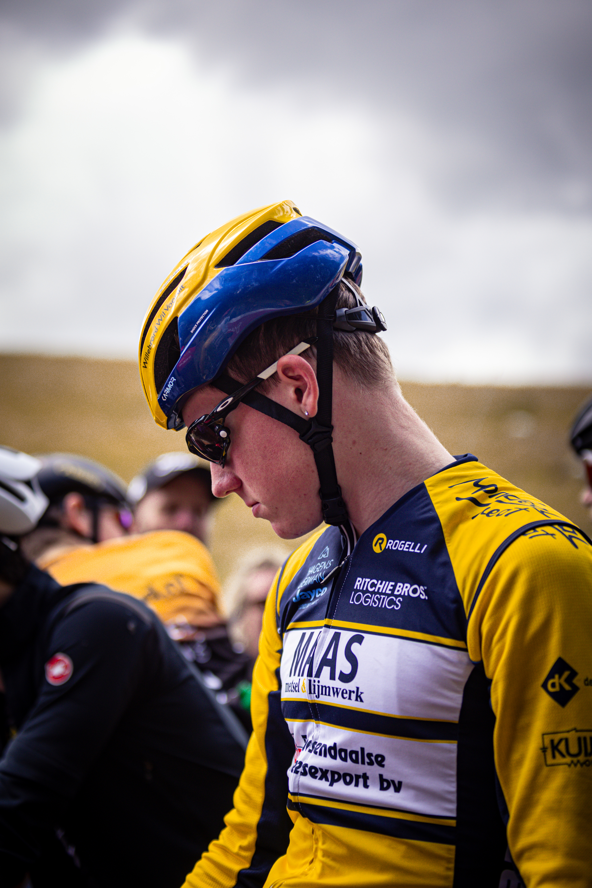 A young man in a cycling race wearing a blue helmet and a yellow and blue jersey.