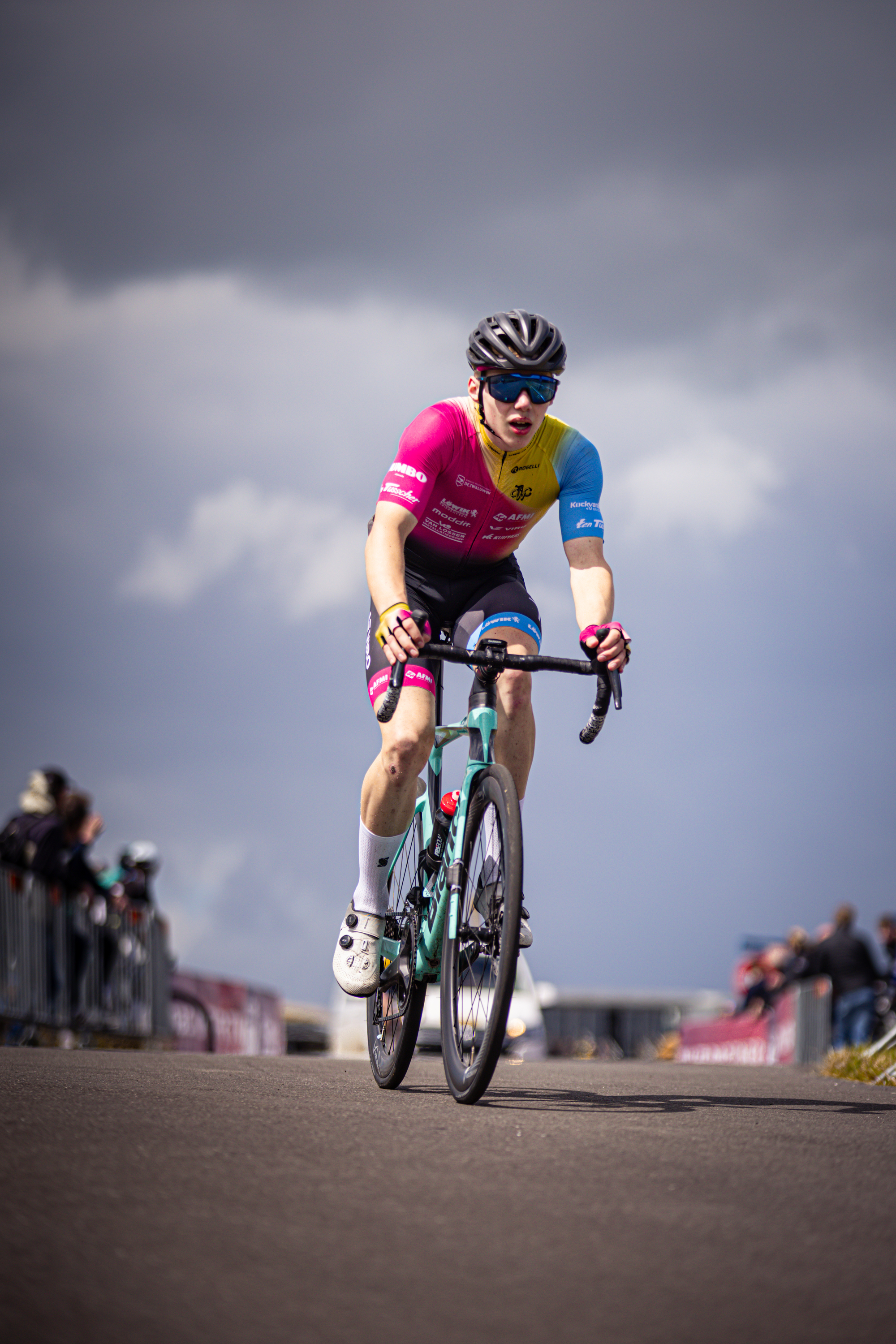 A man in a pink, yellow and blue jersey rides his bicycle on a track.