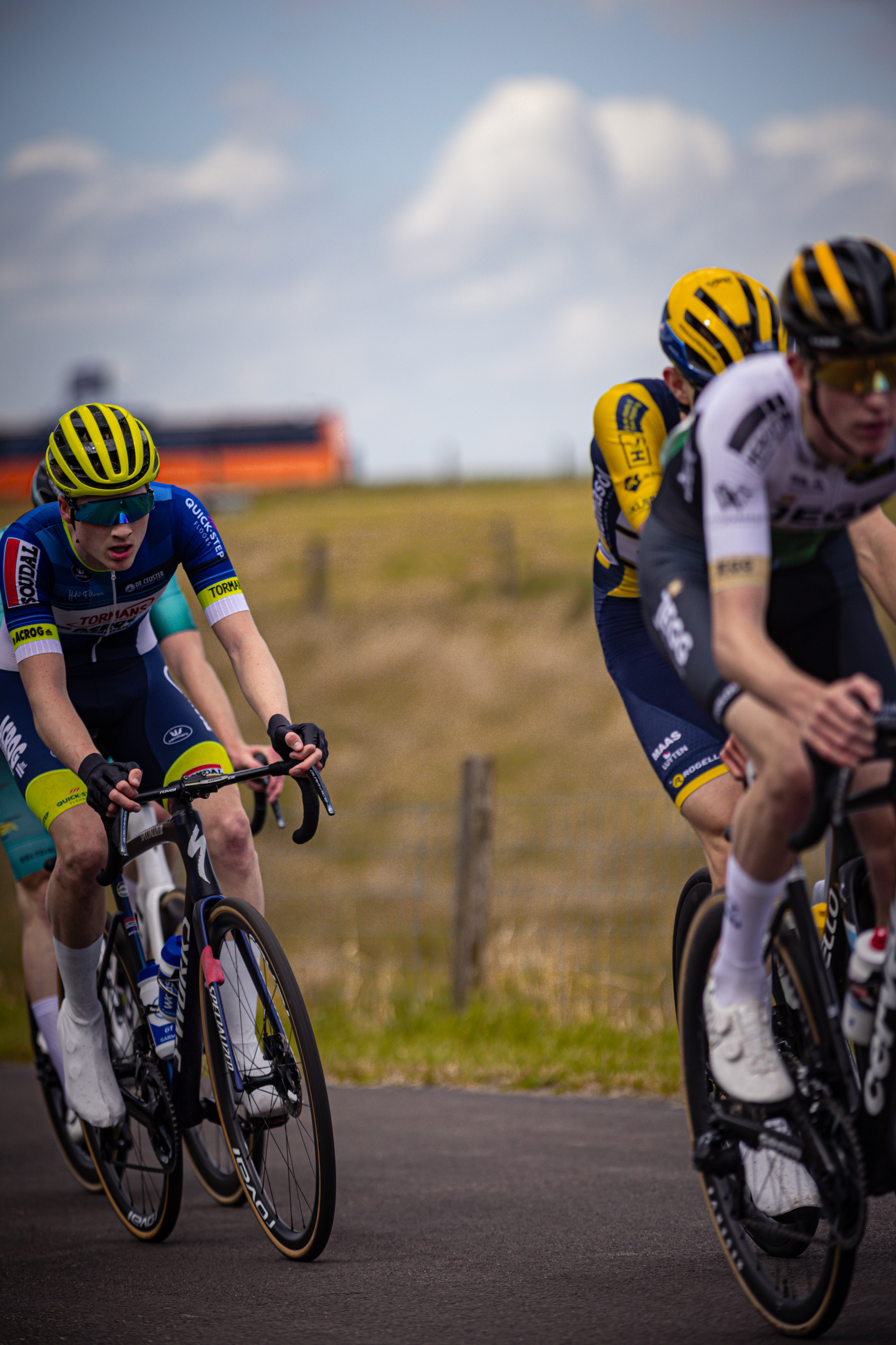 Two cyclists racing each other on a road with a fence in the background.