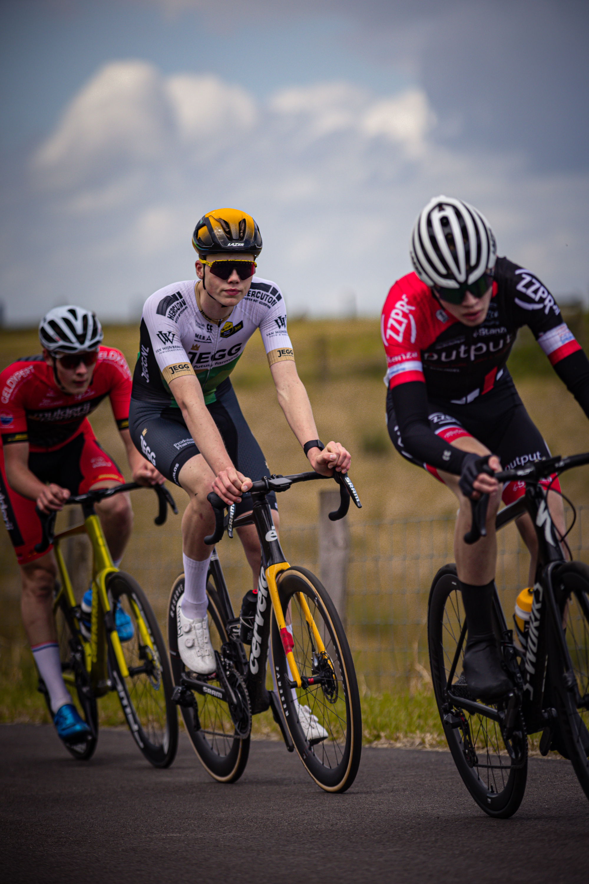 Three cyclists riding on a road, with one wearing a bib that says "Junioren Mannen".