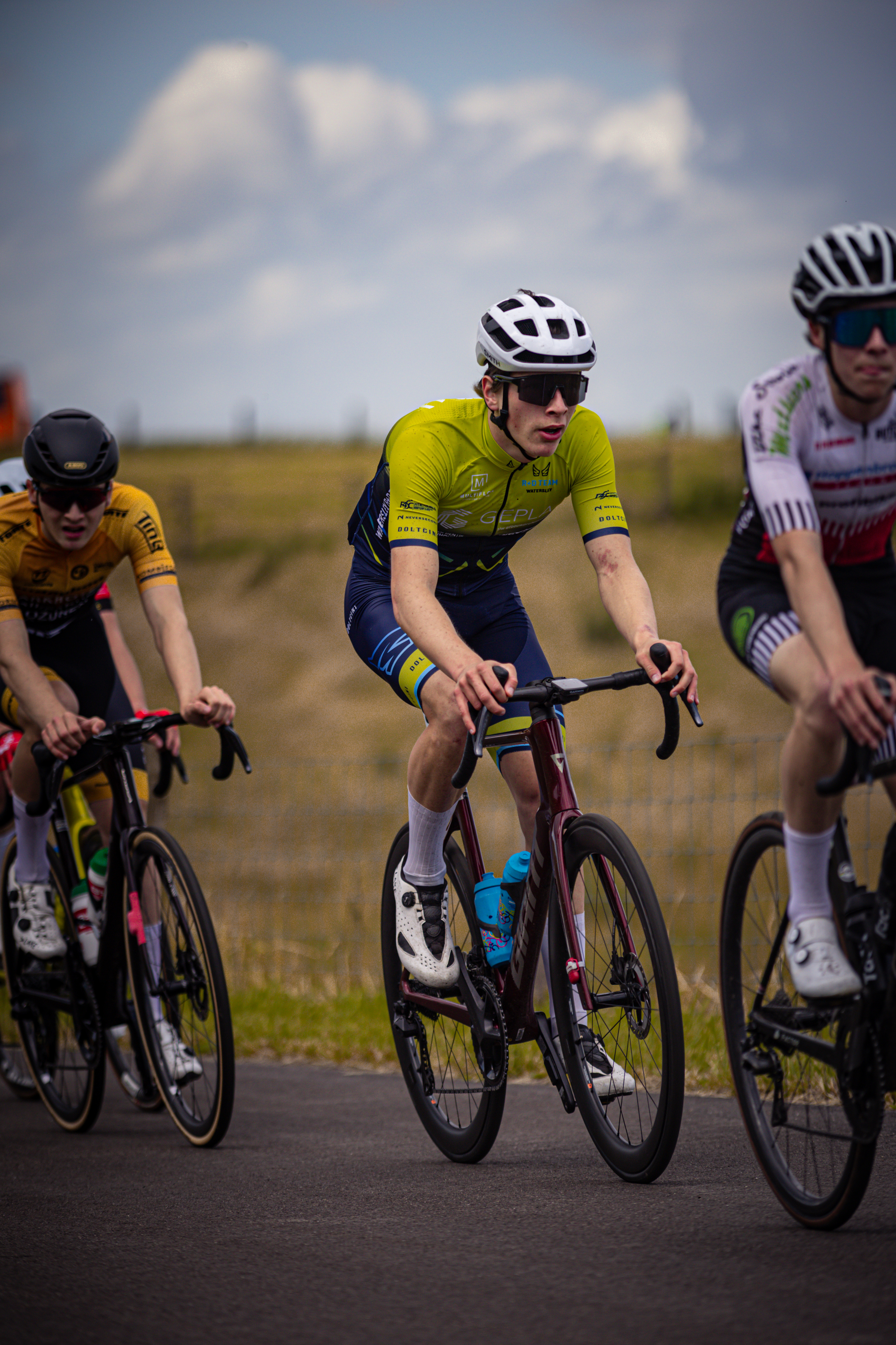 Three young men race on their bikes in a grassy field.