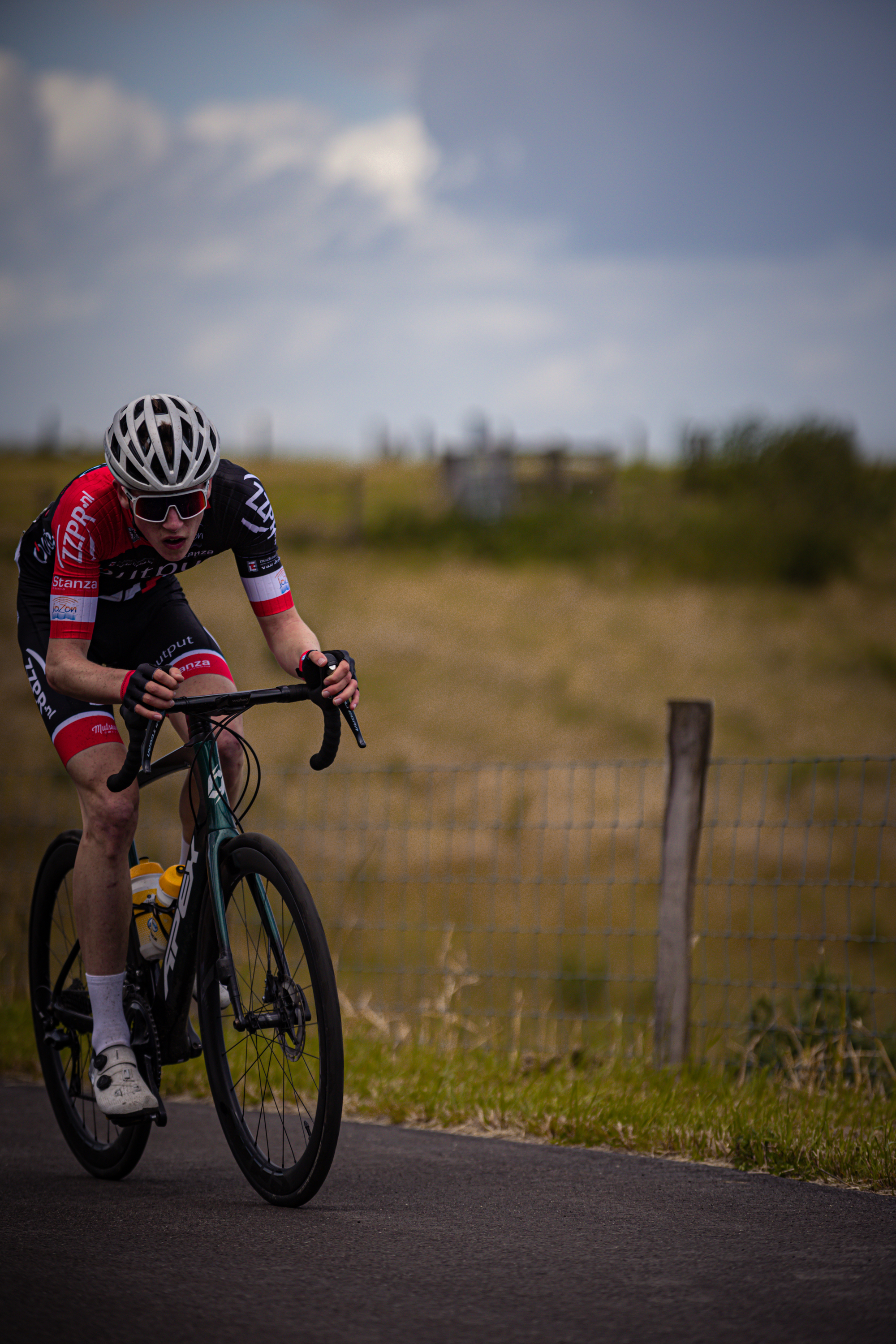 A man with a black and red jersey is riding his bike down the road.