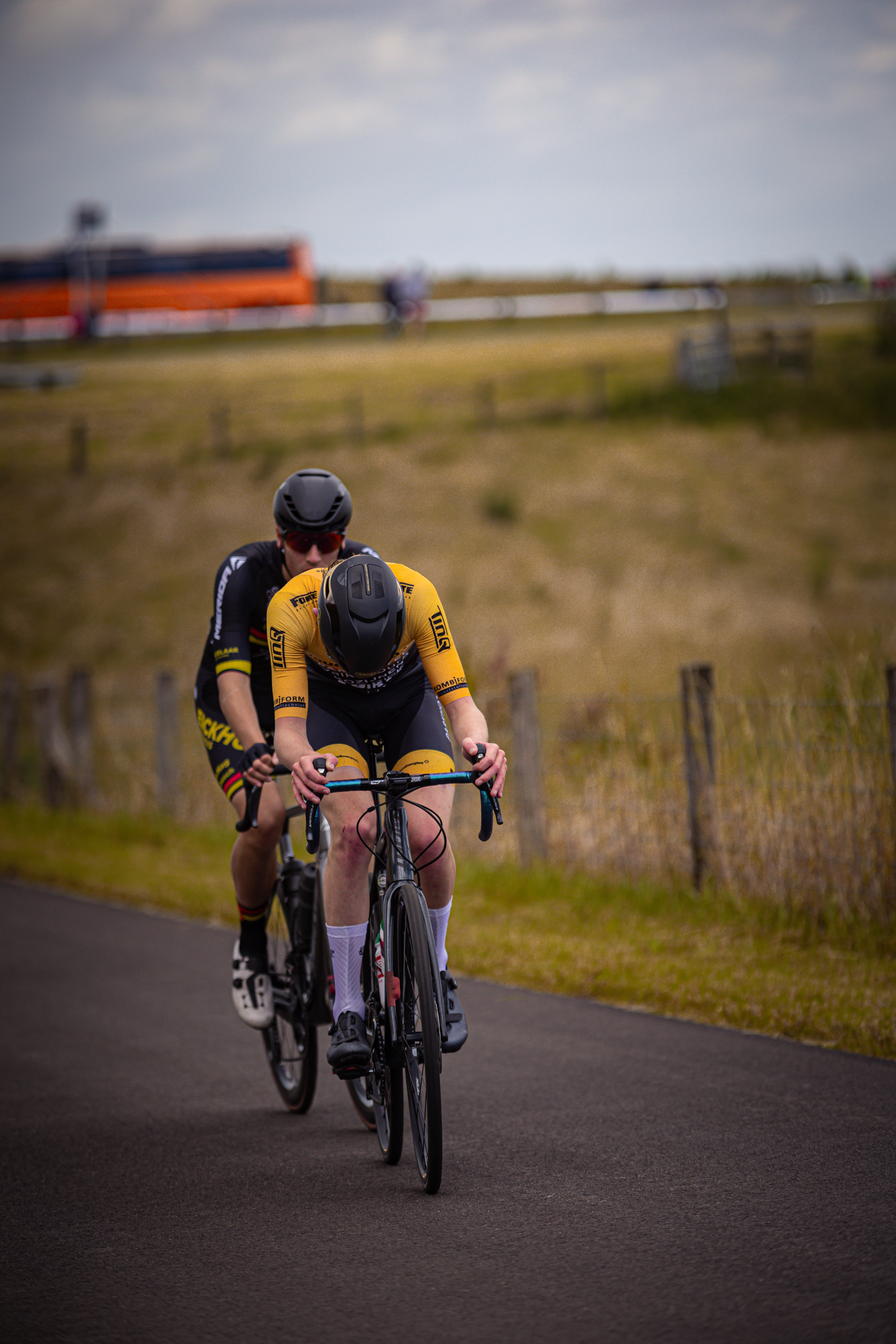 Two cyclists on a road with one wearing an eye mask and a yellow shirt.