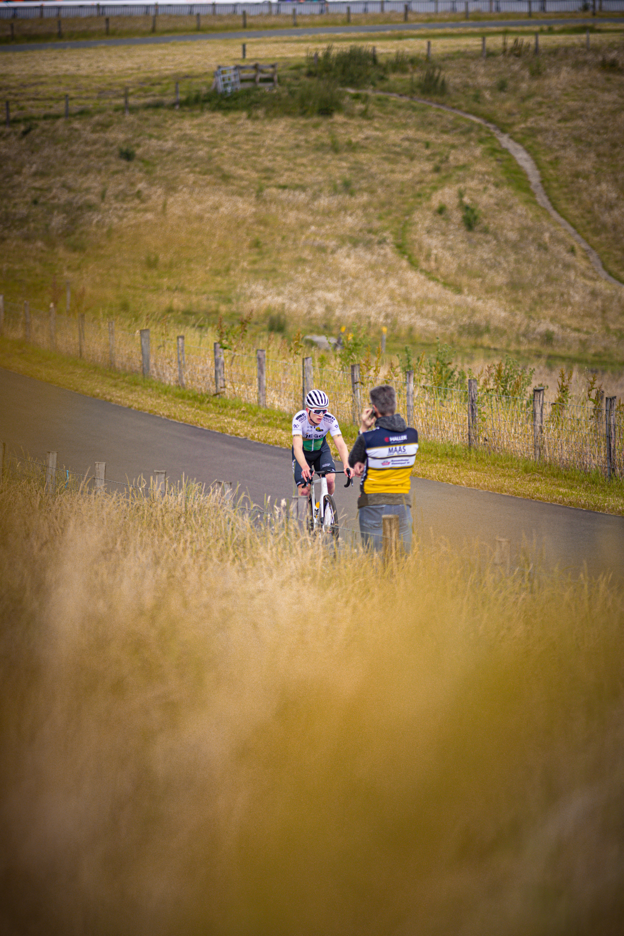 A cyclist is riding on a dirt road next to a man who's watching.