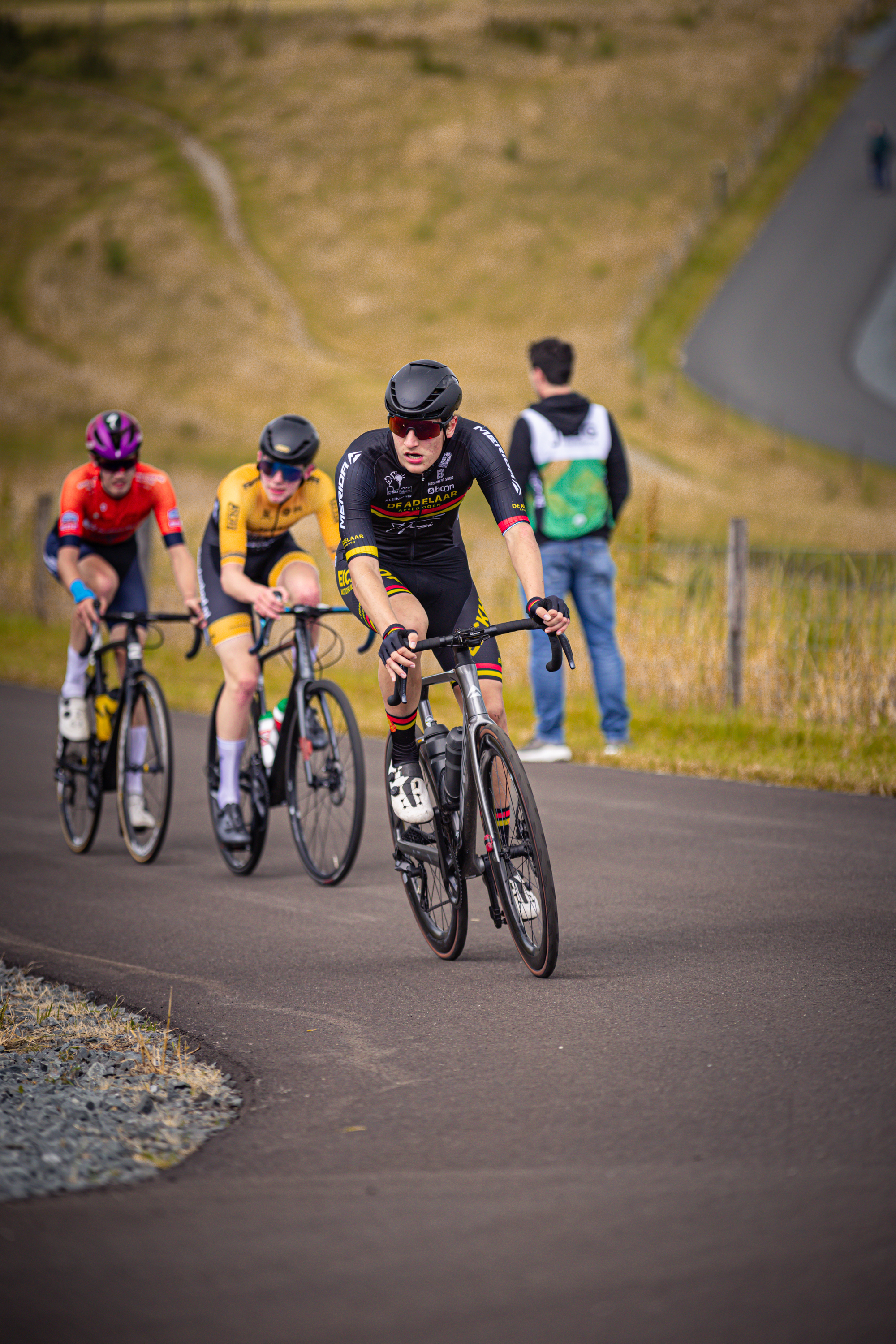 A group of cyclists in a race, wearing helmets and black and red uniforms.