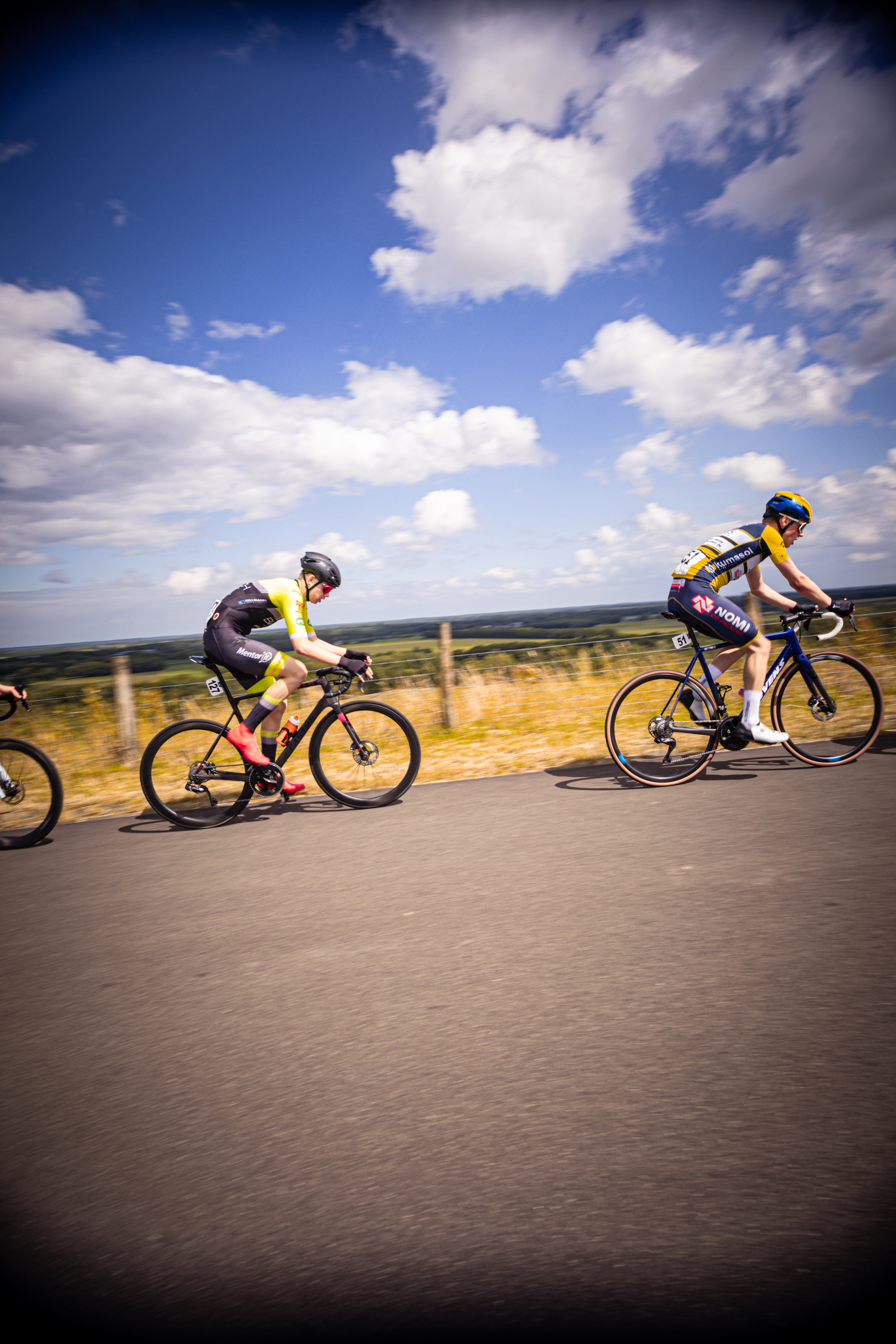 Three people riding bikes on a street with one wearing the number 16 on his back.