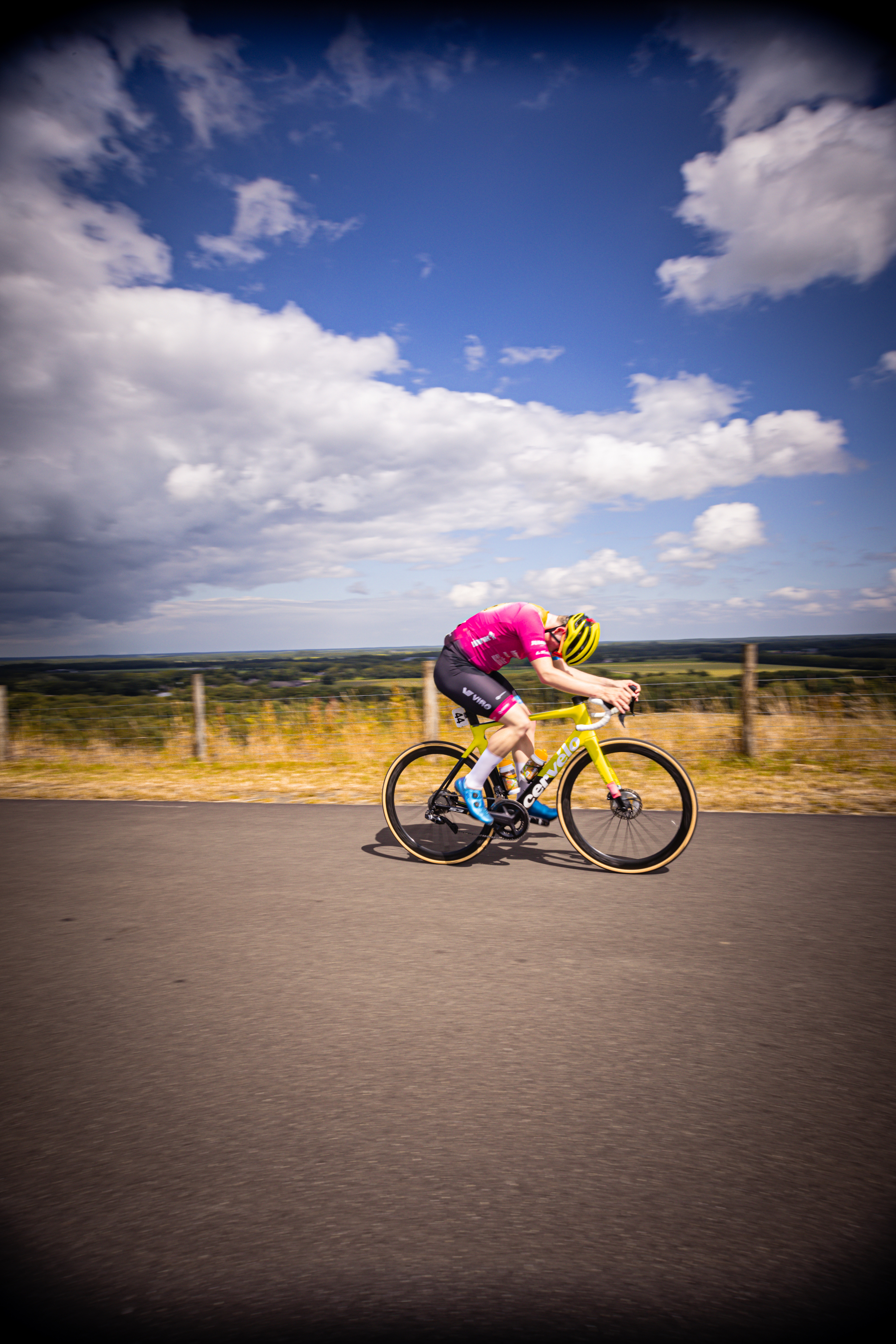 A man in a pink shirt and yellow helmet rides a white bicycle on a road.