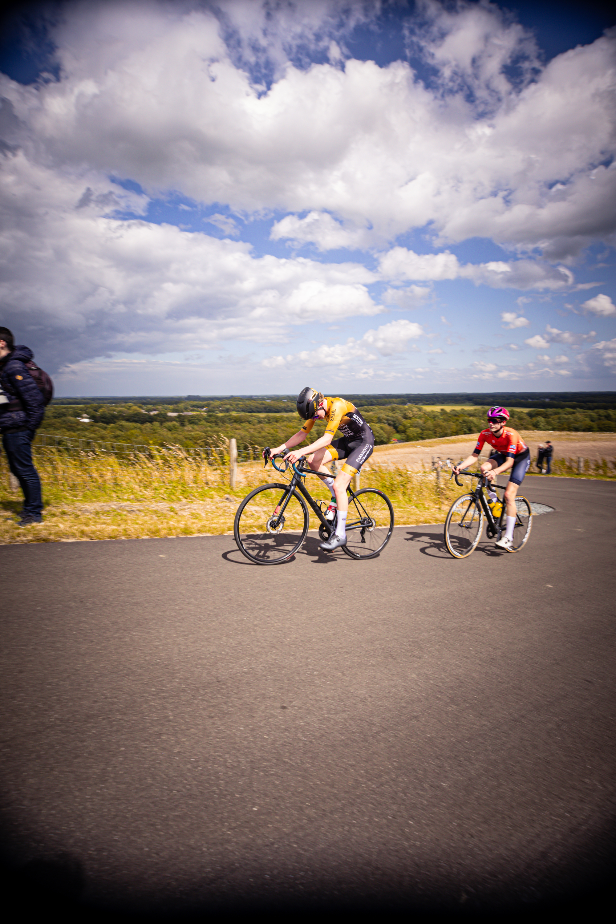 A group of cyclists are on a road near a blue sky.