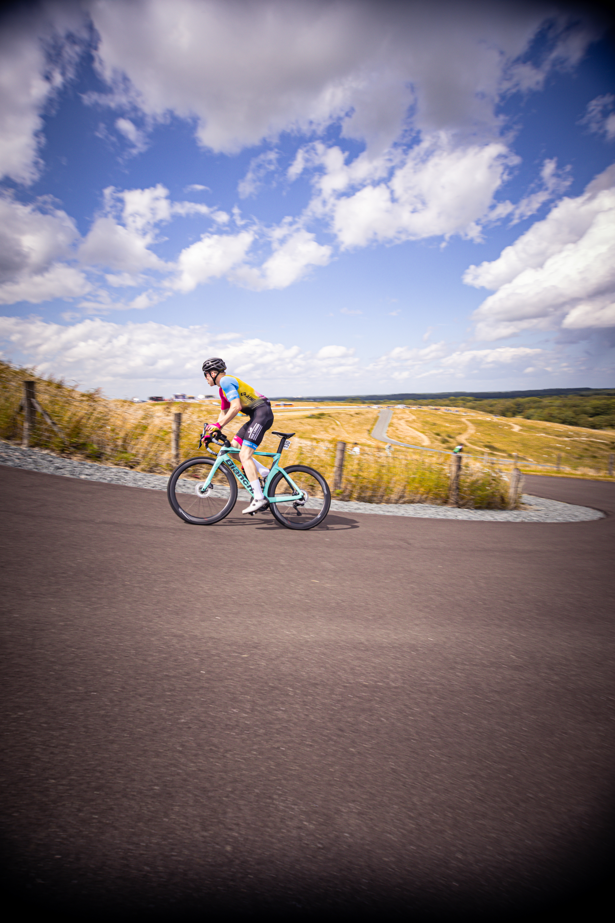 A cyclist in a purple and red jersey is riding a blue bike on a road.