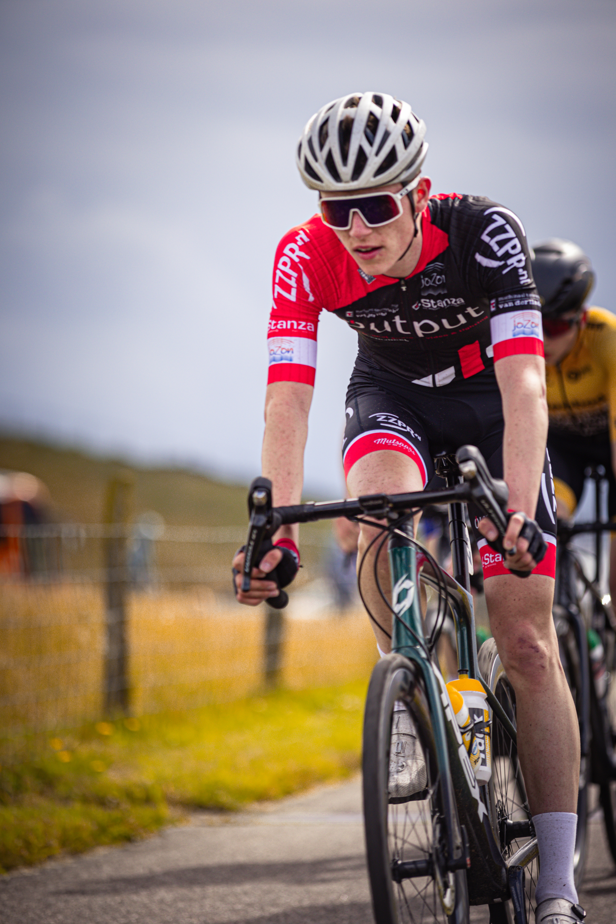 A man in a red and black uniform rides a bicycle with the words "Junioren Mannen" written on it.