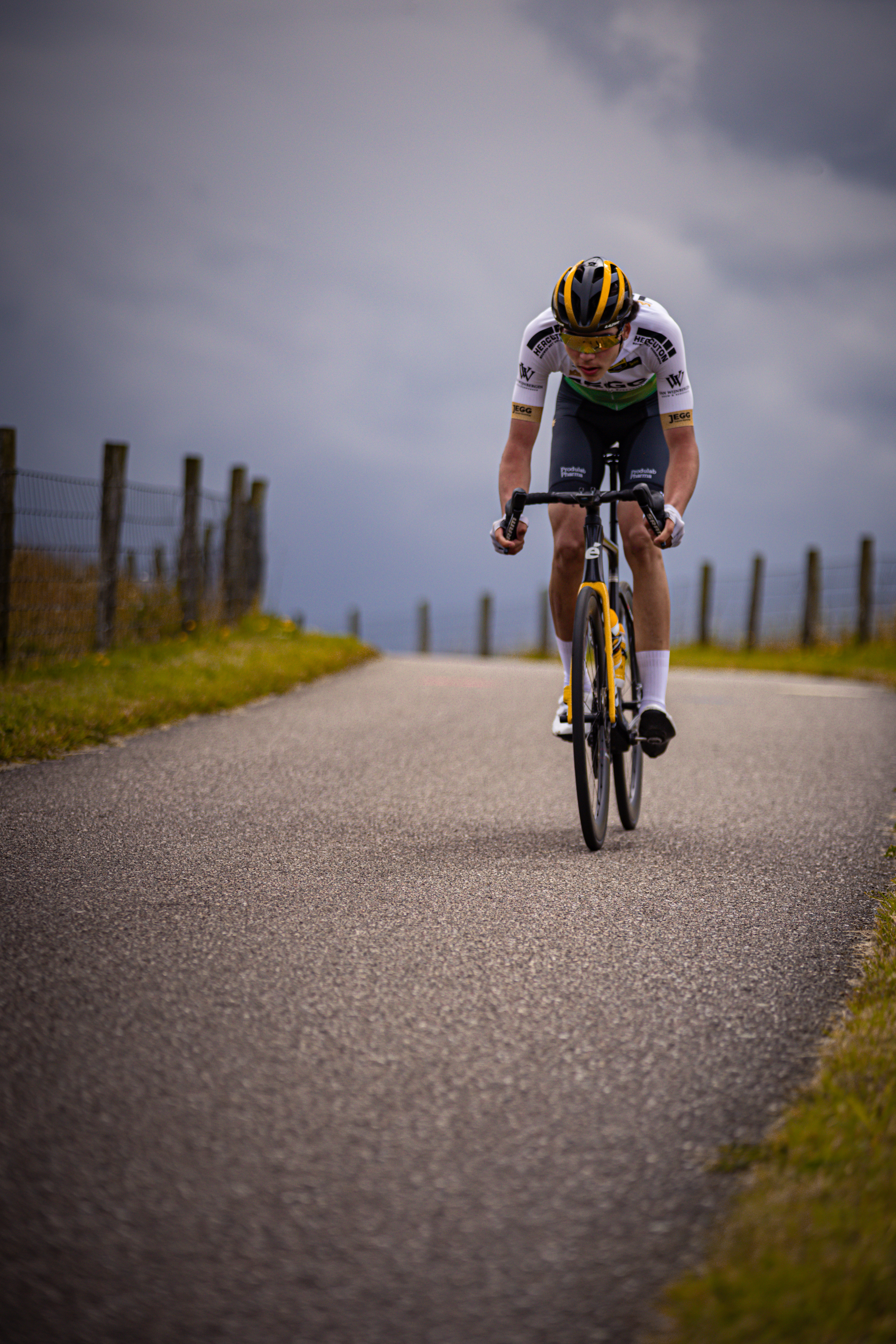 A cyclist wearing a white and blue jersey is riding a yellow bike on the road.