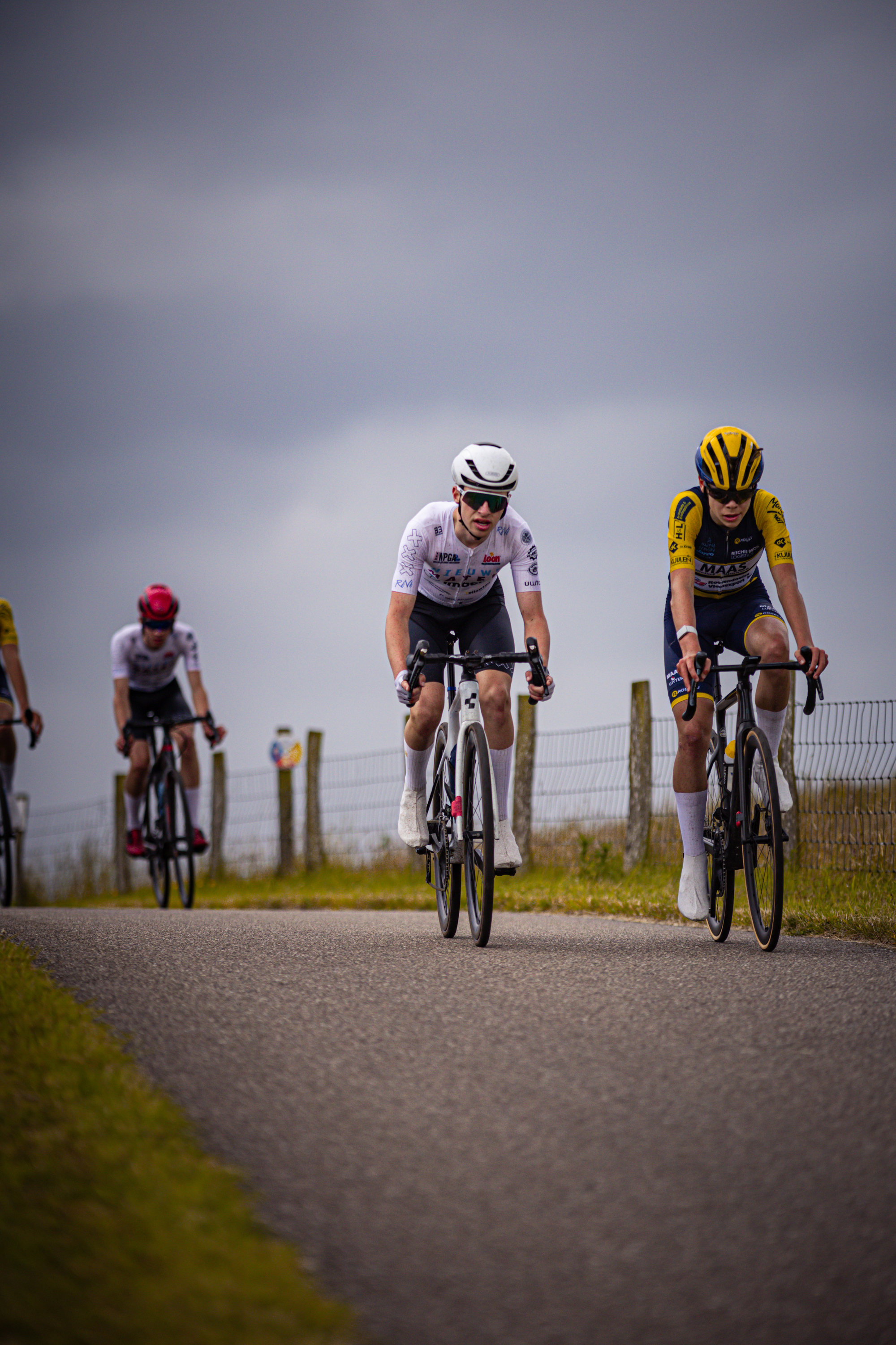 Four cyclists are racing on a track, the lead cyclist is wearing a black suit and has a white helmet.