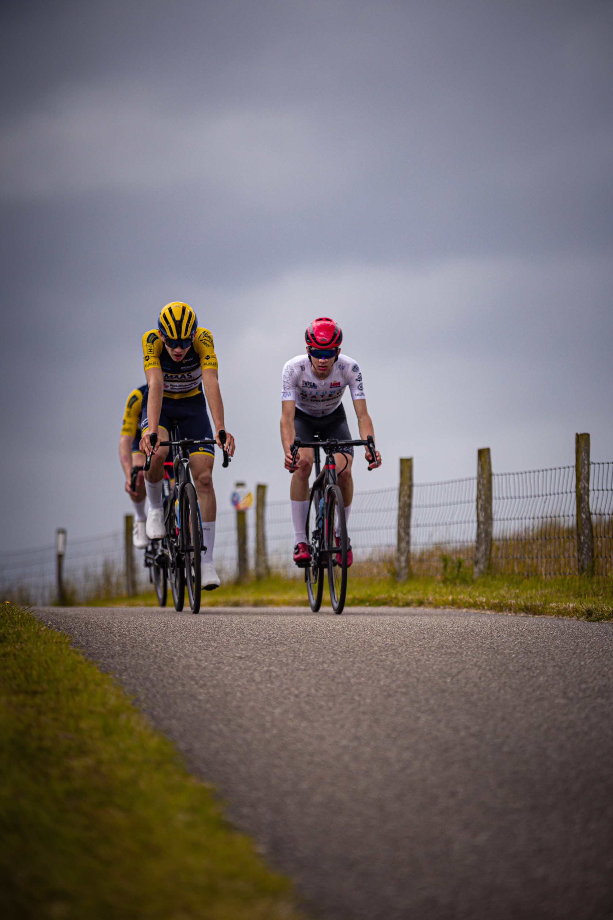 Two cyclists are racing on a road, the man in front is wearing a white jersey.