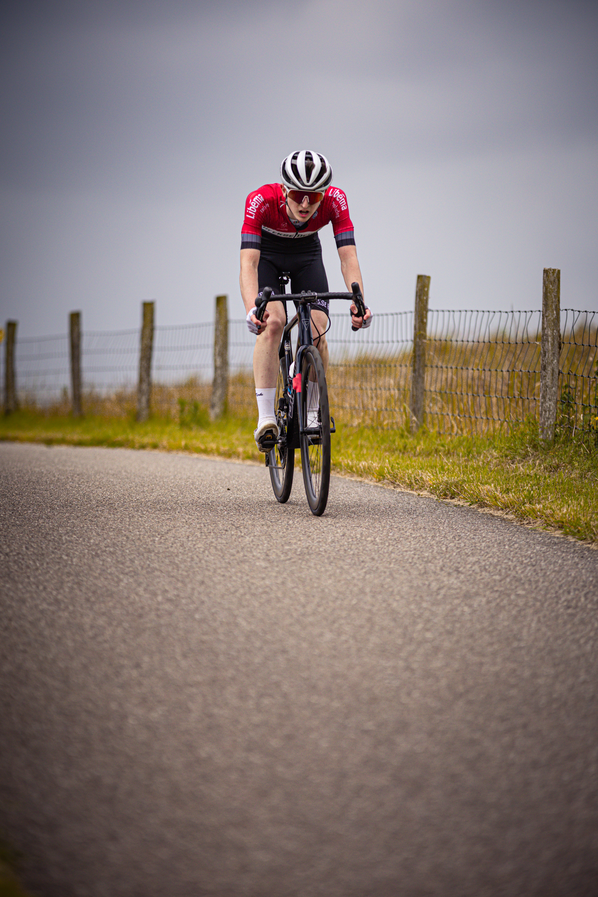 A young man in a red and white jersey is riding his bike down the road, wearing a black helmet.