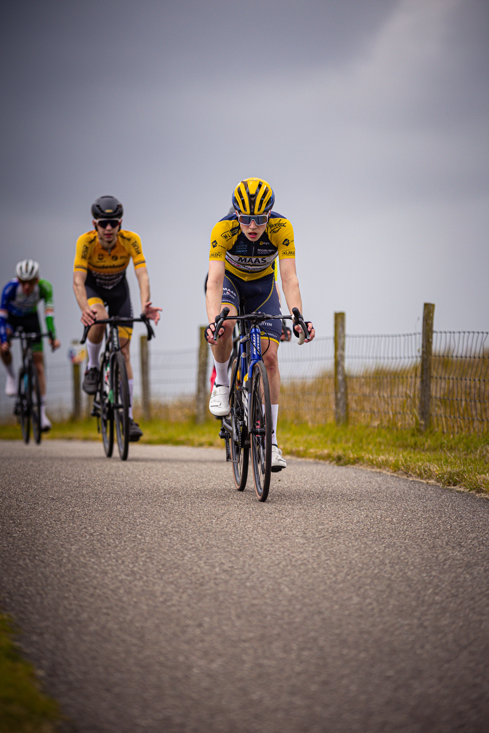 A man in a yellow helmet is riding his bike down a street alongside another cyclist.