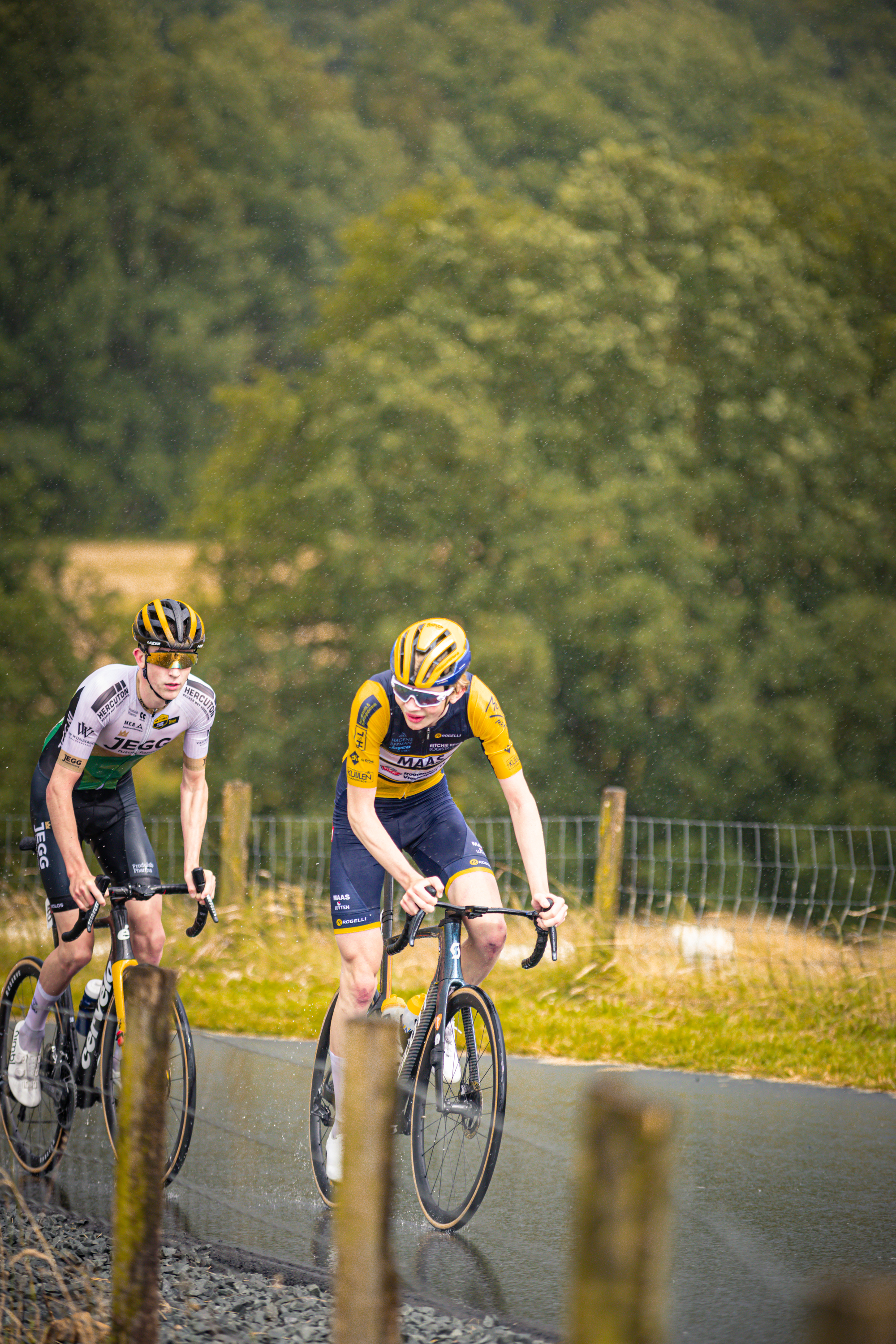 Two cyclists wearing a helmet while riding in the rain.