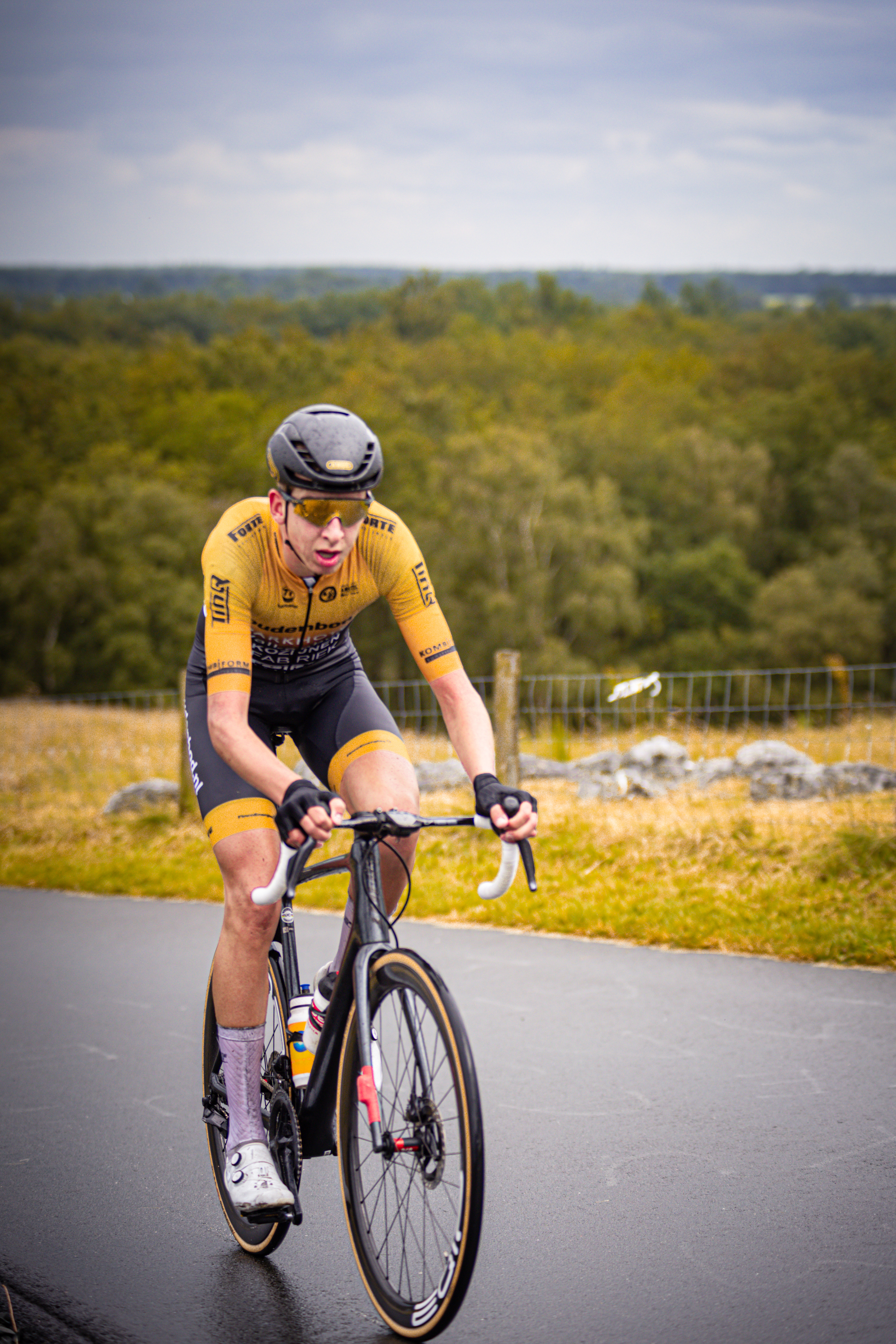 The man is riding a black and orange bicycle while wearing a yellow and black shirt.