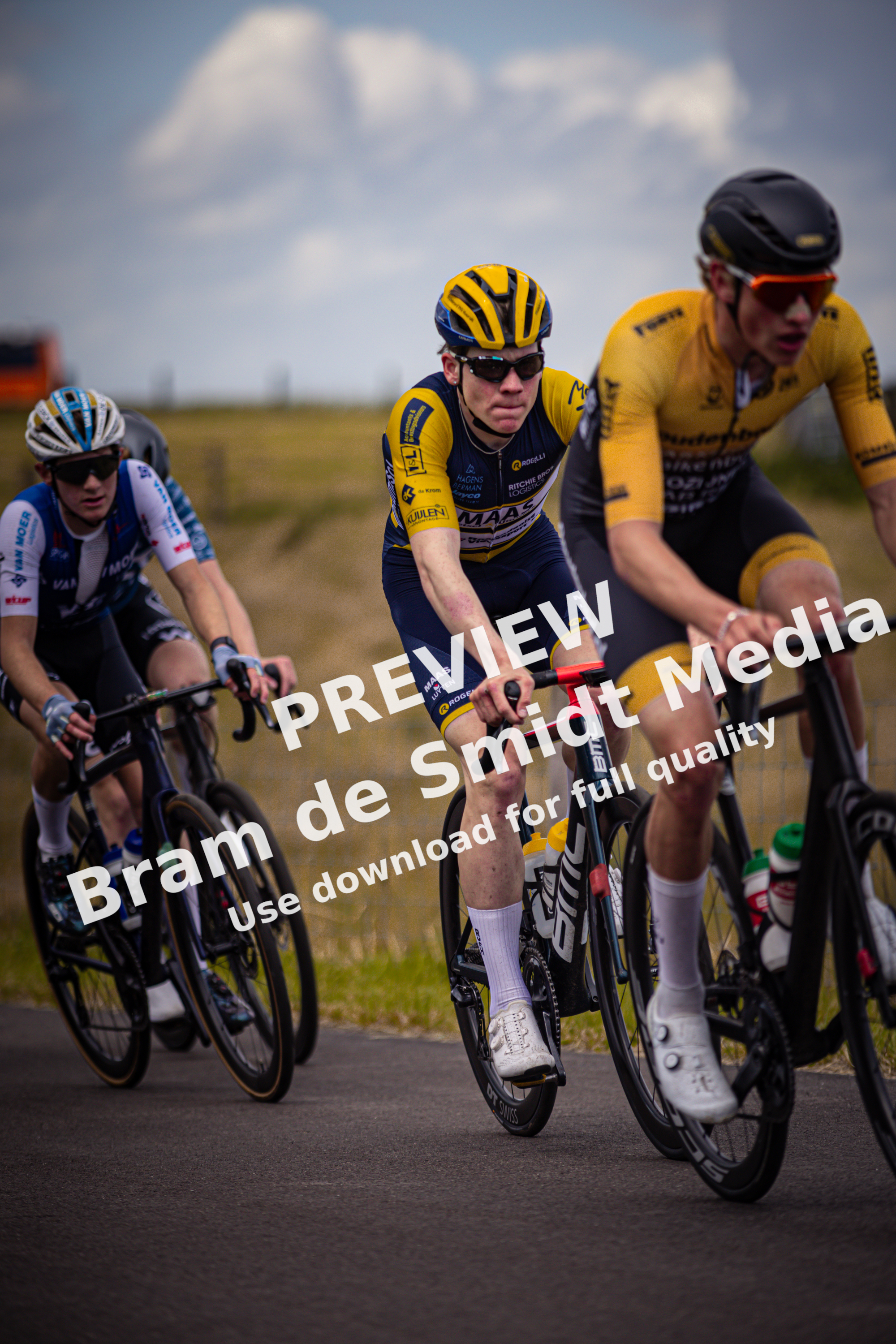 Three cyclists wearing yellow helmets ride on the road.