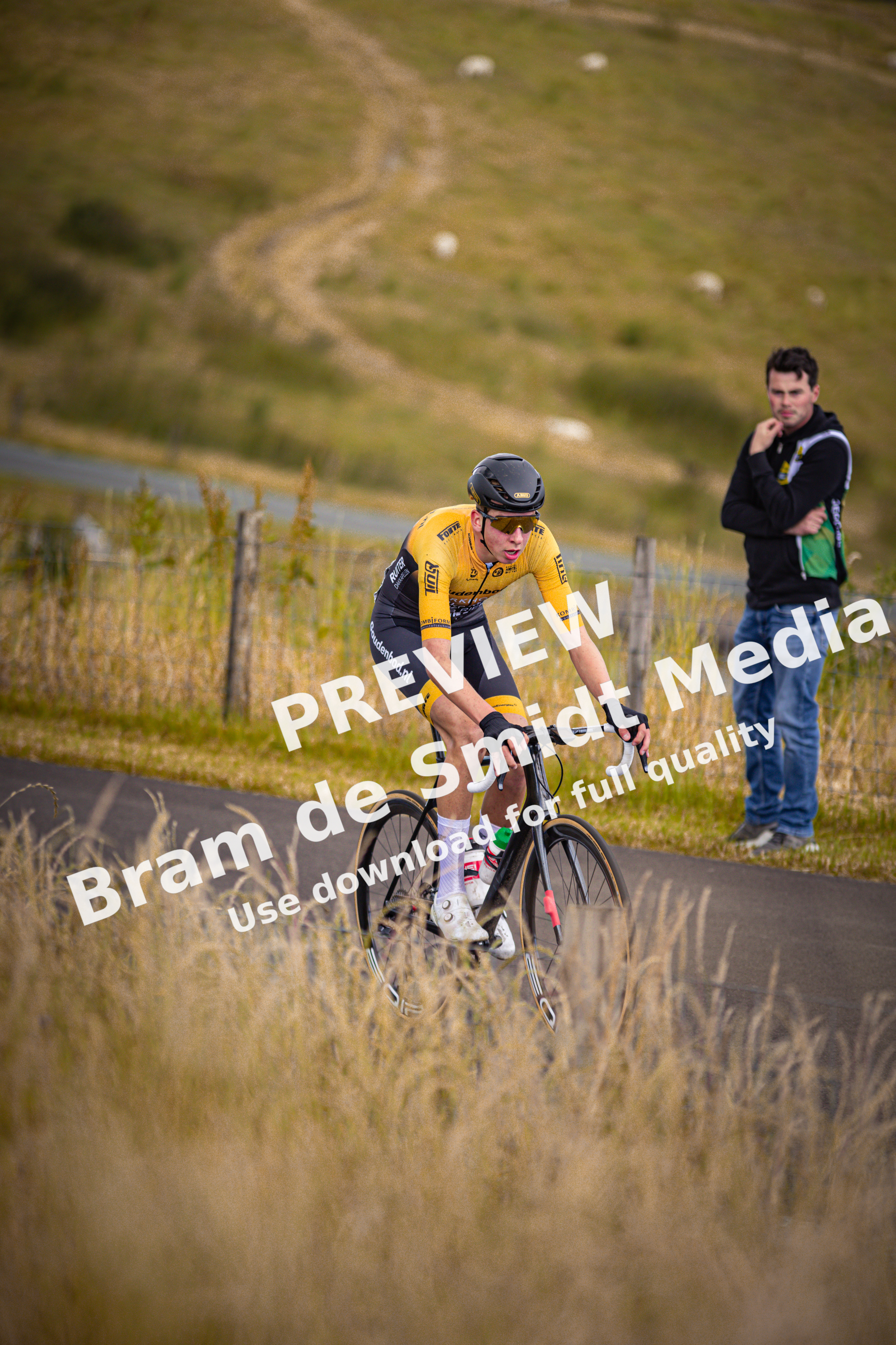 A cyclist in a yellow jersey with number 12 on it rides a bike down the road.