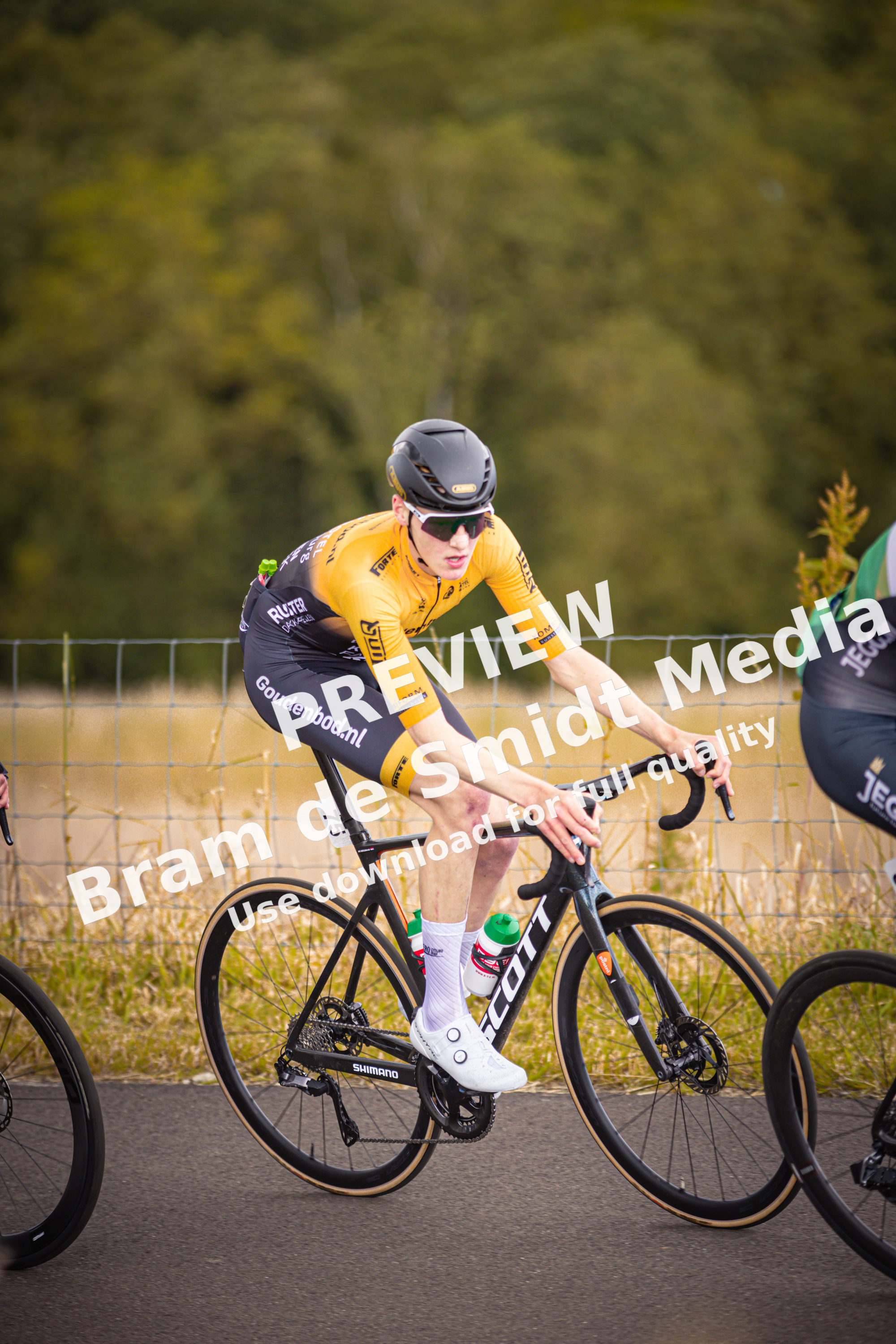 A young man in a yellow shirt and black helmet is riding a bicycle with the word "tijd" on it.