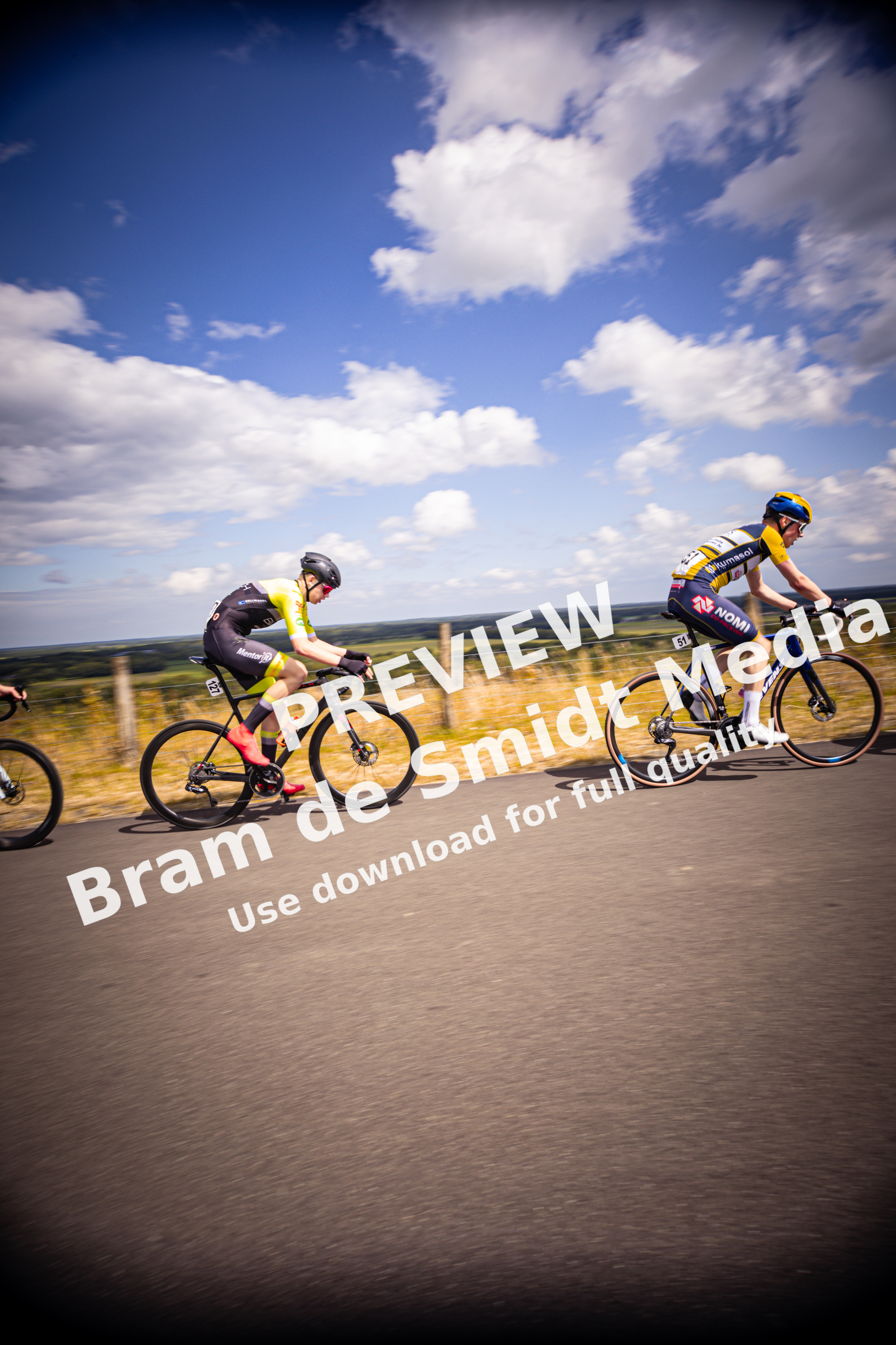 Three people riding bikes on a street with one wearing the number 16 on his back.