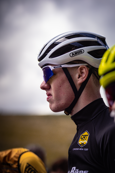 A male cyclist wearing a white bike helmet with the word AEG on it is standing in front of another rider.