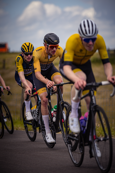 Three cyclists with yellow and black uniforms are racing in a race.