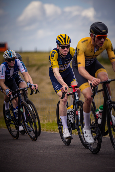 Three cyclists wearing yellow helmets ride on the road.