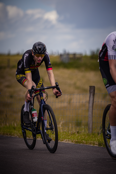 Two cyclists on a road, one of them wearing a black and yellow jersey with the word "Gator" on it.