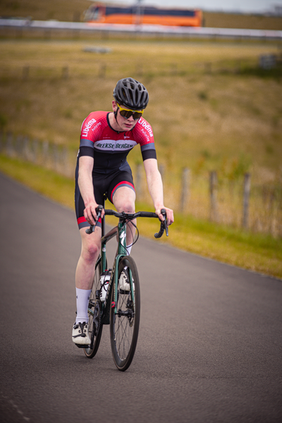 A person wearing a red and black cycling outfit is riding a green bike.