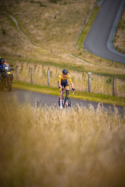 a bike rider on the road wearing a yellow and black jersey with Nederlands Kampioenschap written on it.