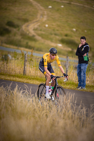 A cyclist in a yellow jersey with number 12 on it rides a bike down the road.