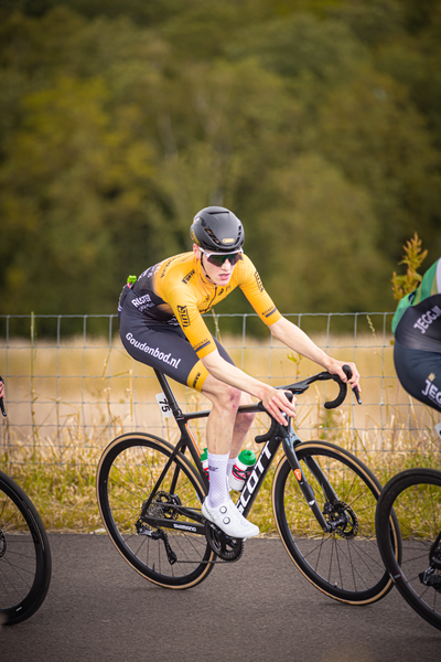 A young man in a yellow shirt and black helmet is riding a bicycle with the word "tijd" on it.